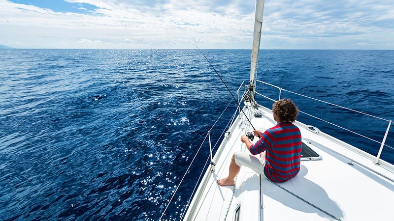 53541510 - man fishing in a calm sea from a sail boat